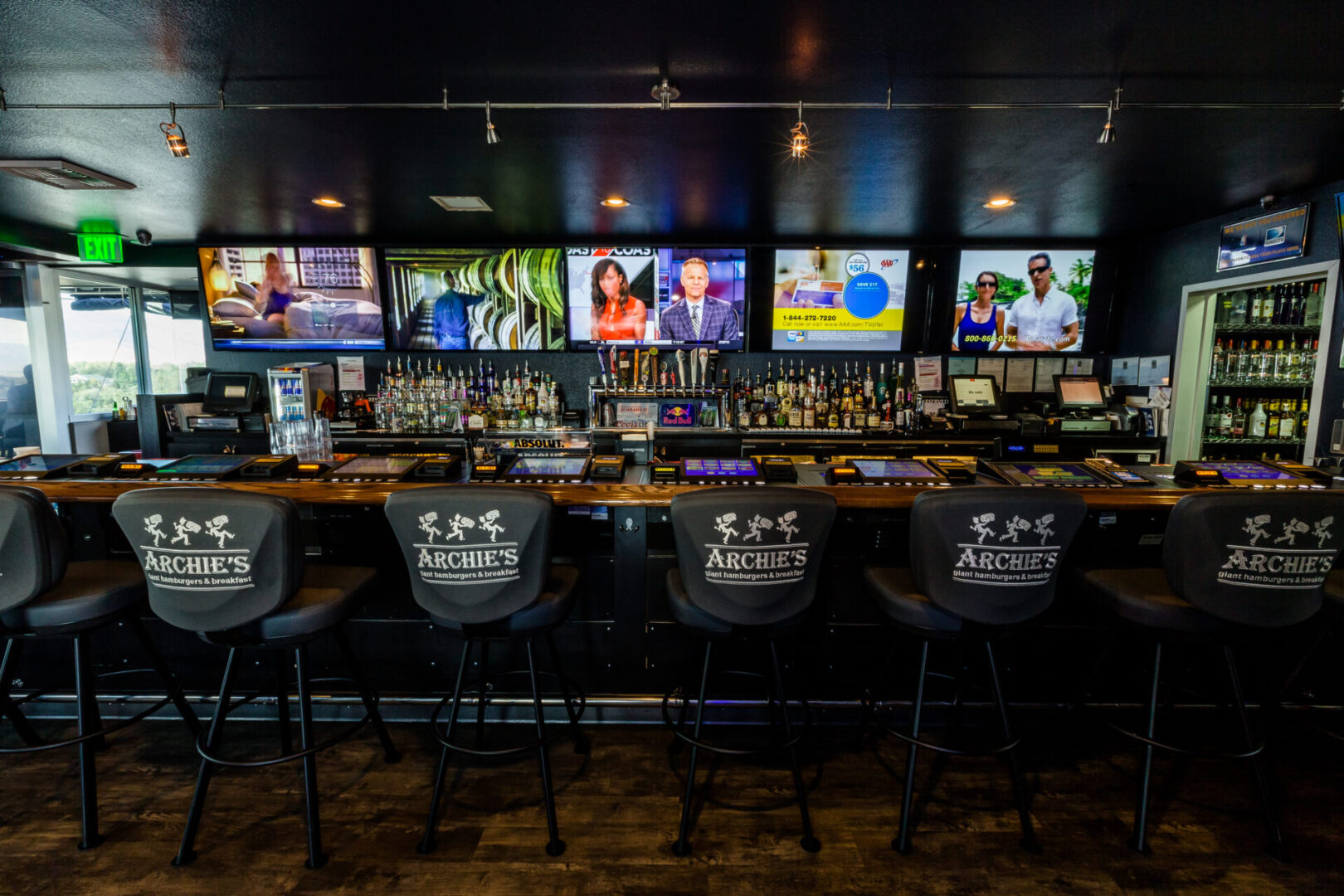 A bar with several chairs and many tvs.