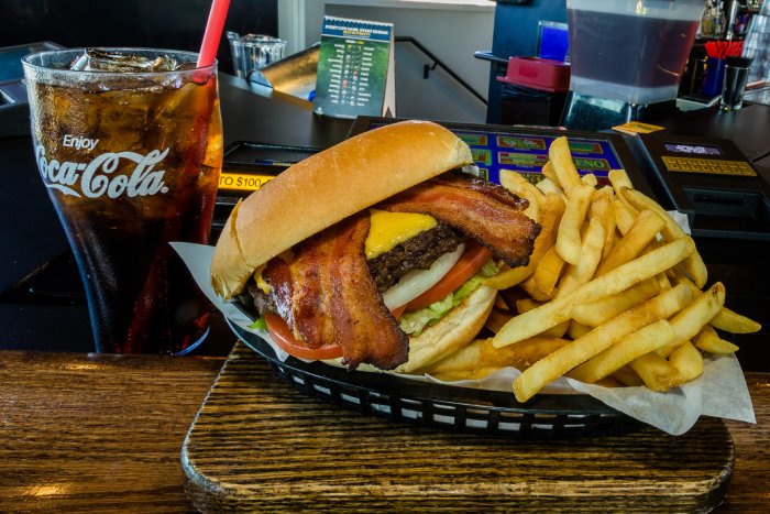 A basket of fries and a bacon sandwich on top of the table.